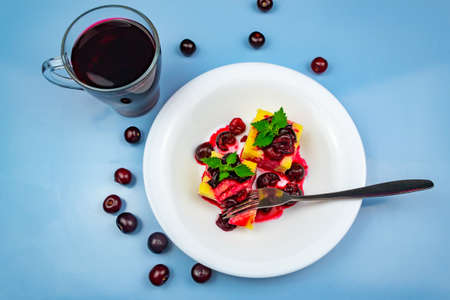 Light breakfast. Two pieces of casserole on a white plate decorated with chopped cherries. A cup of kampot and scattered cherries. Blue backgroundの写真素材
