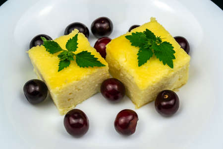 Two pieces of cottage cheese casserole on a white plate, decorated with cherries. Black background