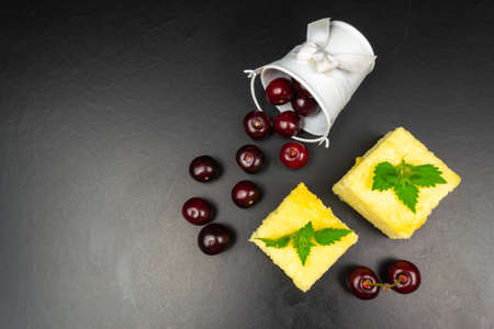 Two pieces of cottage cheese casserole decorated with mint on a black background, a bucket of cherriesの写真素材