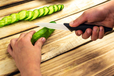 Children's hands are slicing green cucumber, wooden backgroundの写真素材