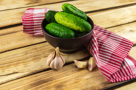 Cucumbers in a brown plate, next to garlic and a red napkin. Wood backgroundの写真素材