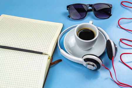 Smartphone with headphones, a cup of coffee notepad pen and glasses with a wristwatch on a blue backgroundの写真素材
