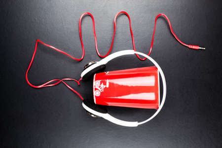 White large headphones are worn on a red cup. Black backgroundの写真素材