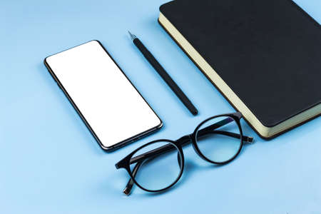 Workspace of a creative office worker. Working with a cup of coffee, using a phone, notepad, pen and glassesの写真素材