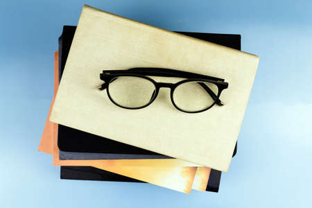 Black-rimmed glasses lie on a pile of books. Blue backgroundの写真素材