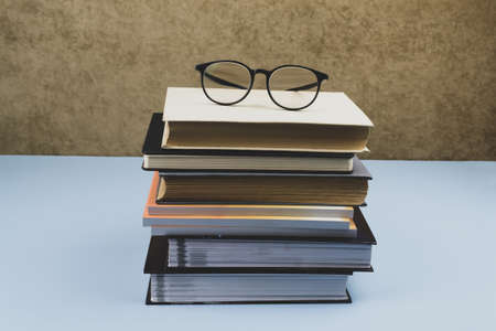 Black-rimmed glasses lie on a pile of books. Blue backgroundの写真素材