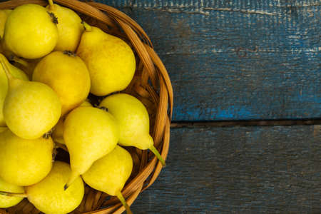 Yellow pears in a wicker plate on a blue backgroundの写真素材