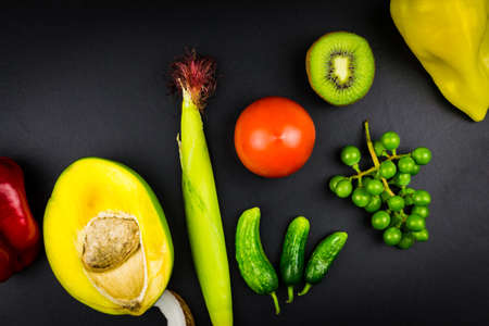 Top view mango corn cucumbers tomato kiwi grapes pepper. Black backgroundの写真素材