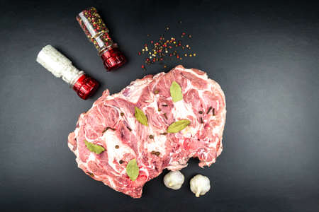 A piece of large fresh raw meat, next to pepper and salt in a mill. Black background