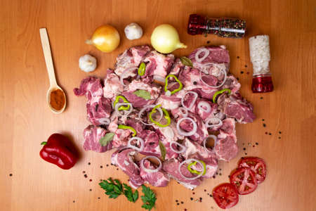 Top view on - Fresh meat cut into pieces, garnished with bell peppers. Potatoes, onions, garlic, paprika in a wooden spoon.の写真素材
