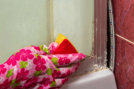Woman's hand in protective rubber gloves using sponge and cleaning shower stall, household chores...