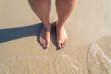 Top view on naked feet on sand in foaming sea wave. Concept of summer holidayの写真素材
