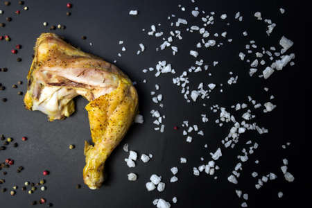 Baked chicken leg pepper and coarse salt, top view on black backgroundの写真素材
