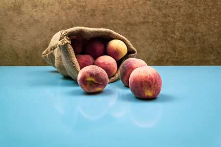 Large ripe juicy peaches fall out of the bag. Blue background close up