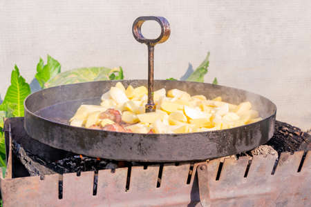 Traditional fried potatoes with pork in a skillet over a fire.