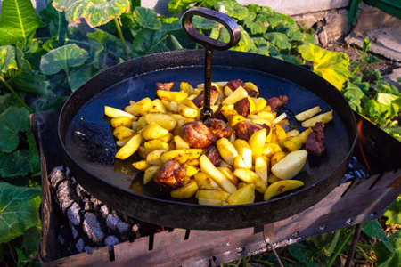 Traditional fried potatoes with pork in a skillet over a fire.の写真素材
