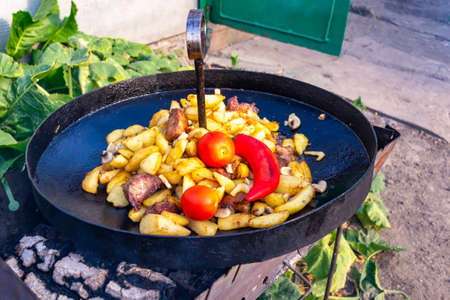 Fried potatoes with pork and mushrooms, garnished with tomatoes and chili in a frying pan over the fire.の写真素材