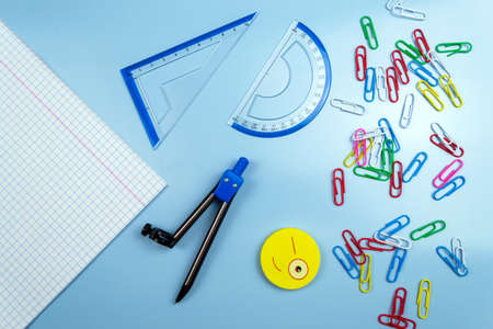 Back to school and education concept. Multi-colored paper clips, rulers, compass, copybook on a blue...