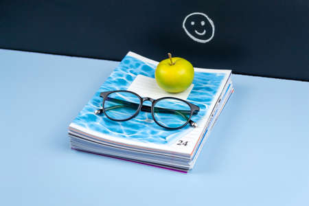 A stack of notebooks are located on the teachers desk near the chalkboardの写真素材