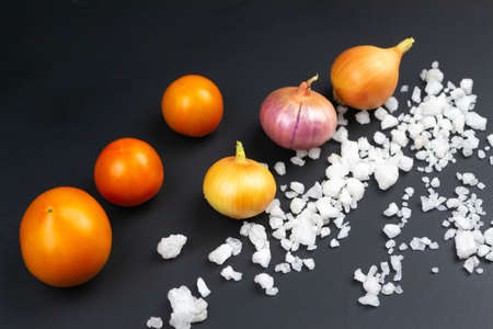 Three red tomatoes, three onions and coarse salt on a black background. Close-upの写真素材