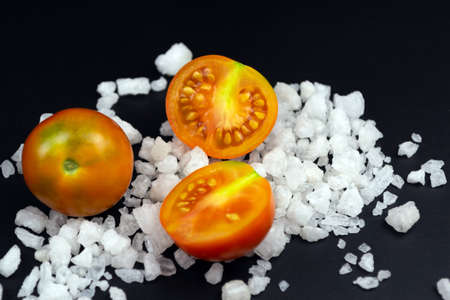 Three red tomatoes on coarse salt on a black background. Close-up