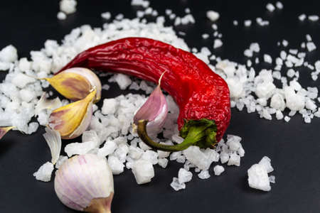 On a black background, cloves of garlic, red chili, traces of coarse sea salt between them.の写真素材