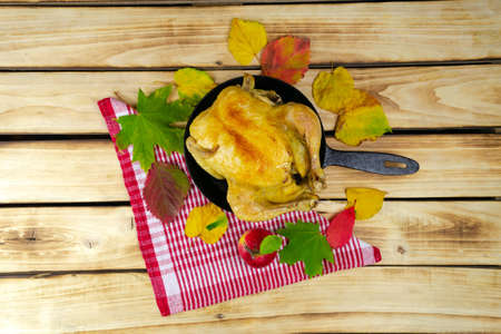 Baked turkey in a frying pan decorated with autumn leaves on a wooden table. Festive autumn theme....