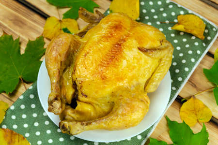 Baked turkey decorated with autumn leaves on a green napkin on a wooden table. Festive autumn theme....