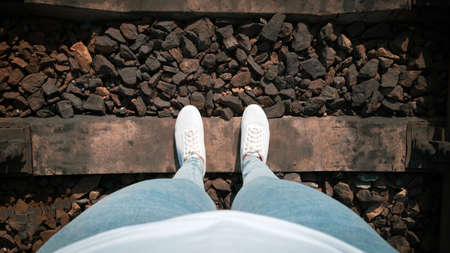 Female legs in jeans and white sneakers on railroad tracks from the first personの写真素材
