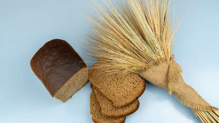 Half loaf of rye bread next to wheat ears on blue background