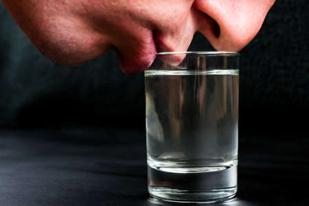 Man touches his lips to a glass of vodka on a black backgroundの写真素材