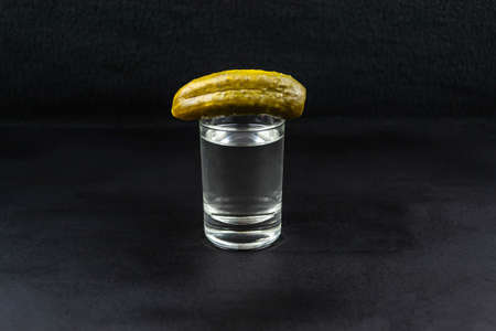 Pickled cucumber on a glass with vodka, on a black backgroundの写真素材
