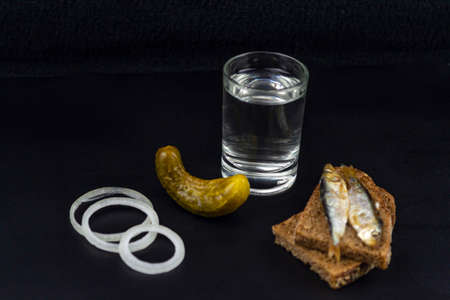 A glass of vodka, two pieces of bread, pickled cucumbers on a black backgroundの写真素材