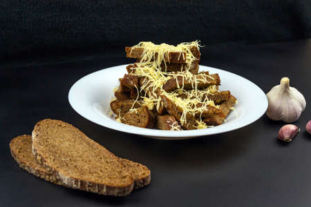 Homemade black bread croutons with garlic and cheese on a black background