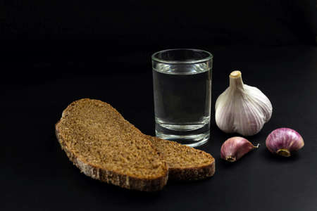 Glass of vodka and garlic on black background