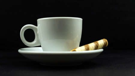 White cup next to crispy striped pipe on black backgroundの写真素材