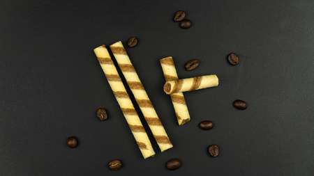 Crispy striped tubes and coffee beans on black backgroundの写真素材