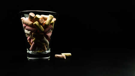 Multicolored little marshmallows in a glass glass on a black background