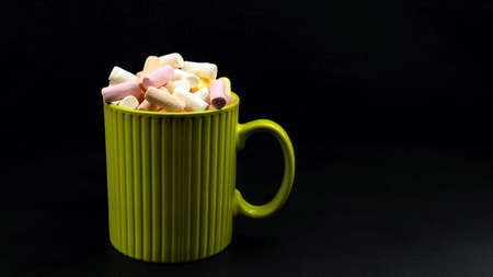 Multicolored little marshmallows in a green cup on a black backgroundの写真素材
