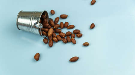 Peanuts falling out of an iron bucket on a blue background