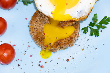 Close up - cut out egg pouring on toast on blue plate with cherry tomatoes and greens