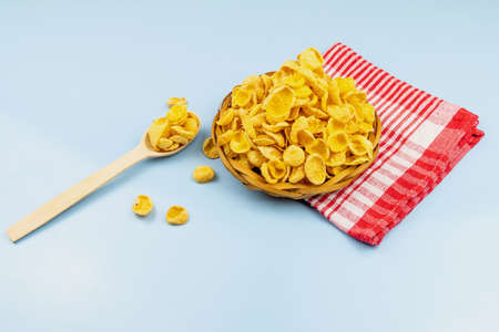 Healthy food cornflakes in wicker bowl with wooden spoon on red towel blue background