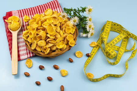 Healthy food cornflakes in wicker plate on red towel with chamomile flower, centimeter tape and...