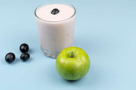 Yogurt in a glass glass with grapes, near a green apple on a blue backgroundの写真素材