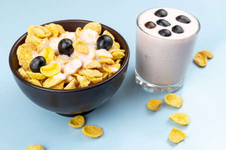 Flakes in a brown clay plate covered with yogurt and a glass of yogurt with grapes on a blue...