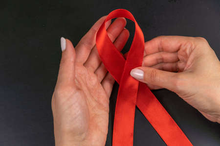 healthcare and medicine concept - female hands holding red AIDS awareness ribbon on black background