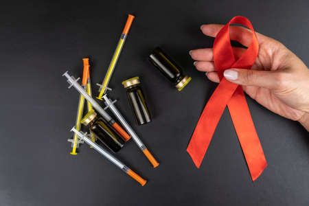 Medical concept, red ribbon symbol of the Day of fight against AIDS in female hands and syringes with ampoules of drugs on a black backgroundの写真素材