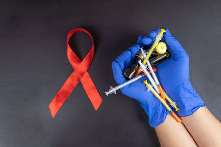 Medical concept, red ribbon-symbol of the Day of fight against AIDS and in women's hands syringes...