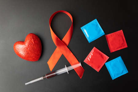 Multicolored condoms syringe red heart and red ribbon aids day on black background