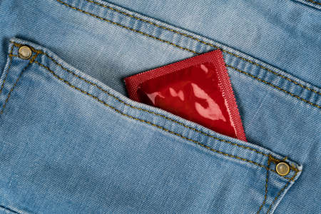 Red condom in blue jeans pocket close-upの写真素材